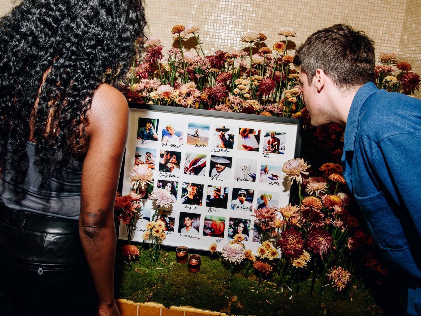 Guests viewing a wall of signed Fire Island polaroids framed in flowers
